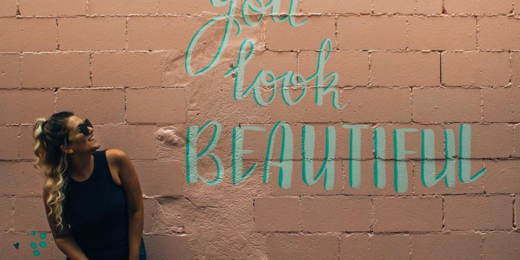 A stylish woman with curly hair and sunglasses poses beside a vibrant mural in Toronto.