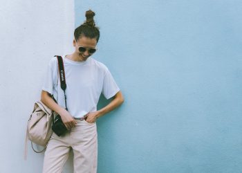 Stylish woman posing with camera in casual attire against a blue wall.