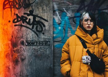Young woman in yellow winter jacket against vibrant graffiti wall, conveying urban street style.