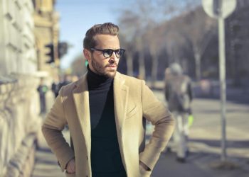 Stylish man in glasses and coat posing outdoors on an urban street in Budapest.