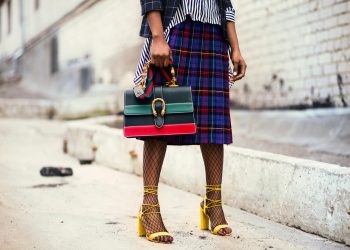 Fashion-forward outfit with plaid skirt and colorful handbag in urban setting.