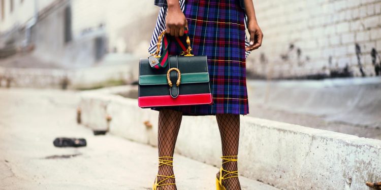 Fashion-forward outfit with plaid skirt and colorful handbag in urban setting.