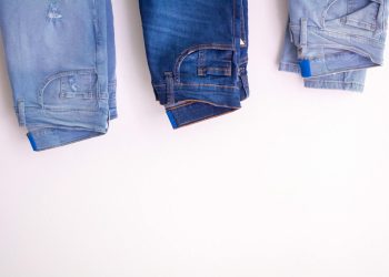 Three pairs of denim jeans neatly folded and hanging against a white backdrop.