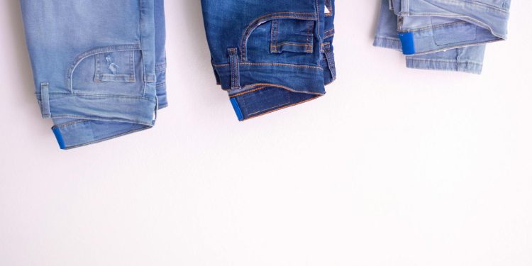 Three pairs of denim jeans neatly folded and hanging against a white backdrop.