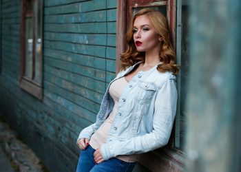Stylish woman with red lipstick poses against a rustic wooden wall, exuding urban charm.
