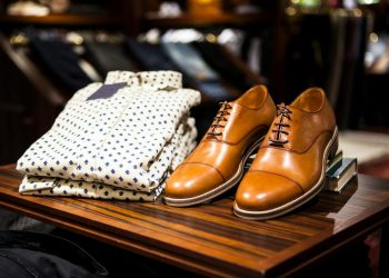 Elegant brown leather shoes and printed shirt displayed on a wooden table in a stylish clothing store.