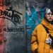 Young woman in yellow winter jacket against vibrant graffiti wall, conveying urban street style.