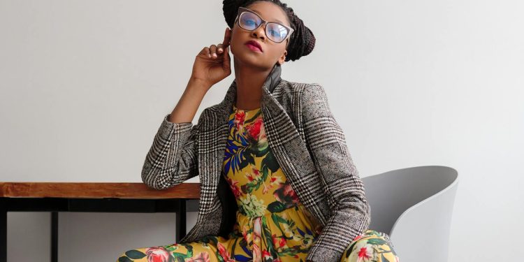 Elegant woman posing in a modern setting, wearing a floral dress and eyeglasses.
