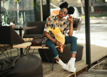 Trendy woman with sunglasses and flowers relaxing on a patio bench in sunlight.
